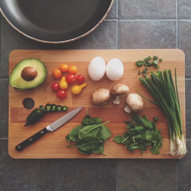 Fresh vegetables, eggs and a knife laid out on a cutting board