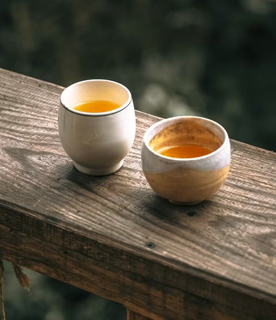 Two cups of tea side by side on a wooden railing